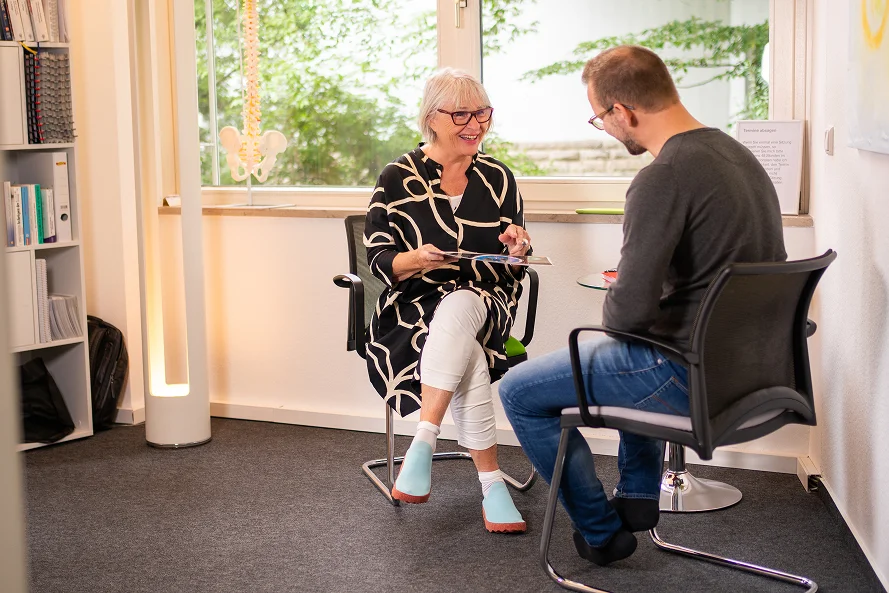 Ute Weisshaar sitzt mit einem Patienten in einem Praxisraum